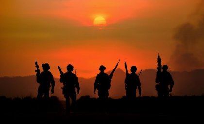 A group of soldiers with weapons silhouetted against a smoky red sky